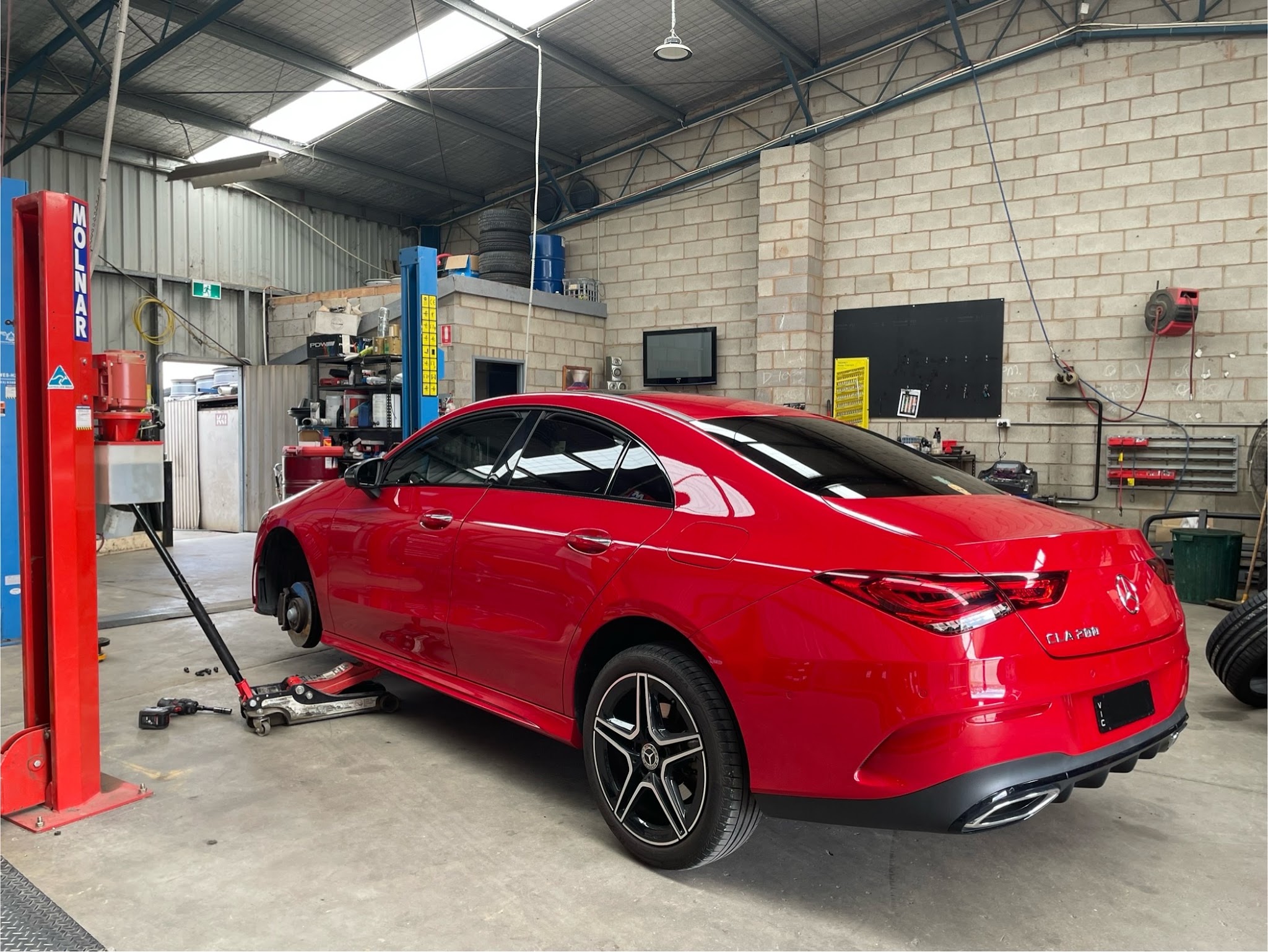 A car up on the jack in the Sunday Tyres workshop beside the two post hoist