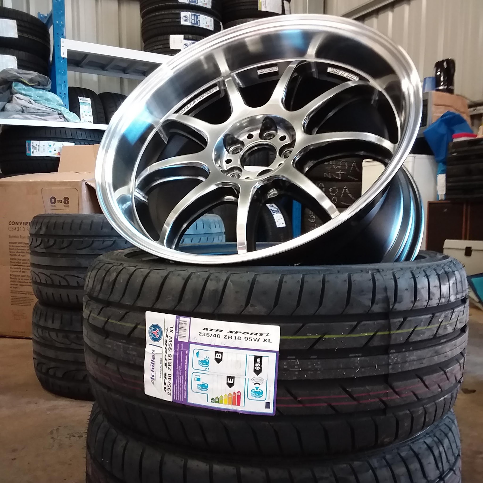 Polished alloy wheel resting on a stack of new performance tyres in the store